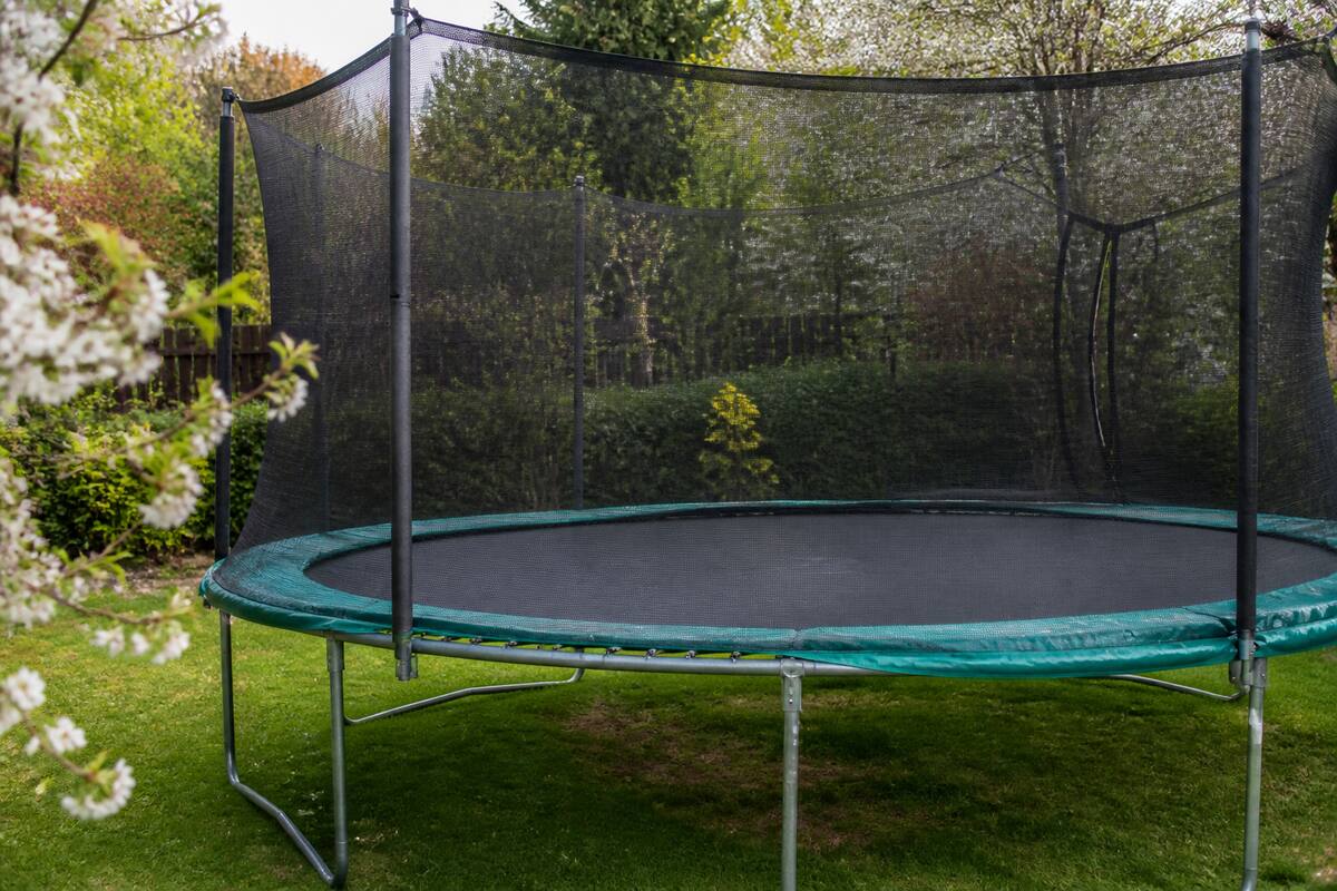Trampoline in een tuin met zicht op springmat, randkussen en veiligheidsnet